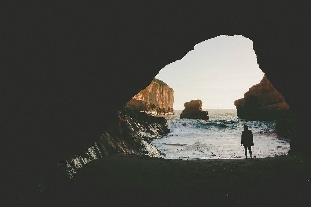 Person standing on the cave entrance looking at the ocean bay. Original public domain image from Wikimedia Commons