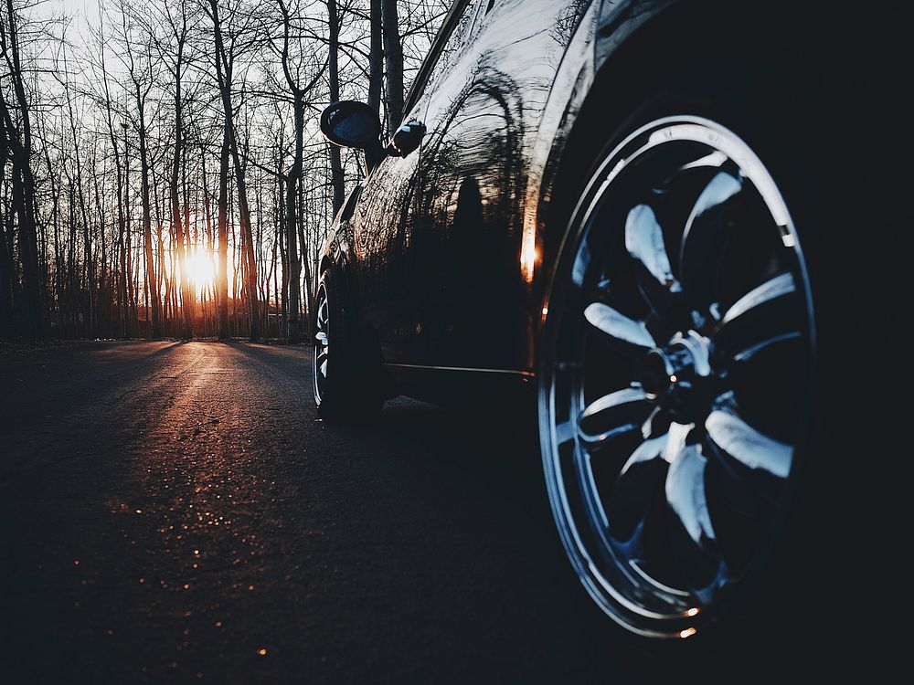 Black car chrome rim on an asphalt road in a leafless forest on sunset. Original public domain image from Wikimedia Commons