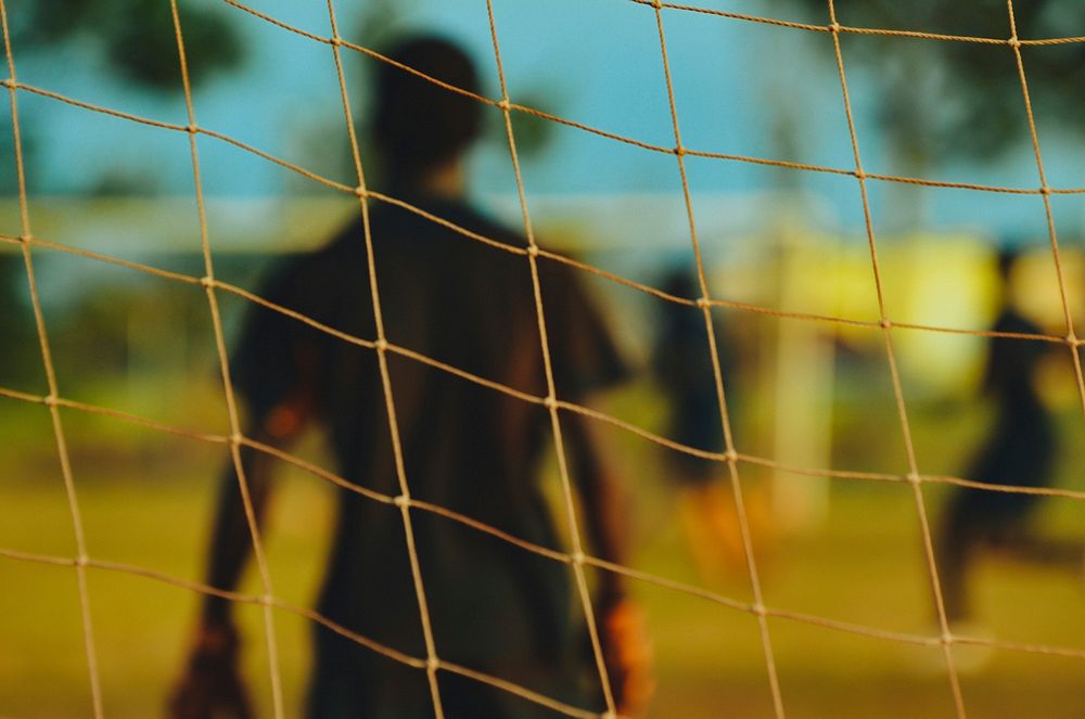Blurred goalkeeper through the focused goal net in New York, Texas.. Original public domain image from Wikimedia Commons