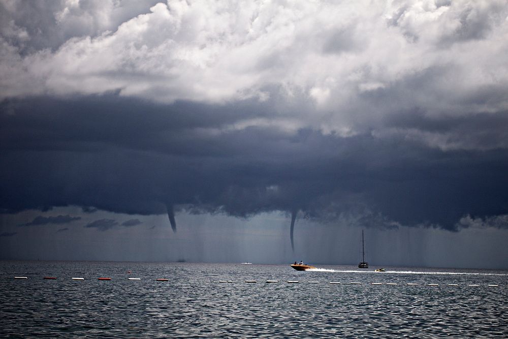 Speedboat speeding across the sea with waterspout tornadoes in the distance in Budva Municipality. Original public domain…