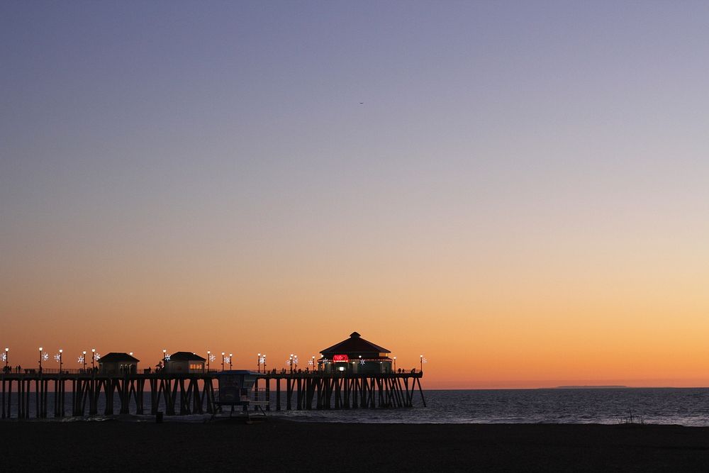 The sun setting behind the twinkling lights of the Huntington Beach pier, California. Original public domain image from…
