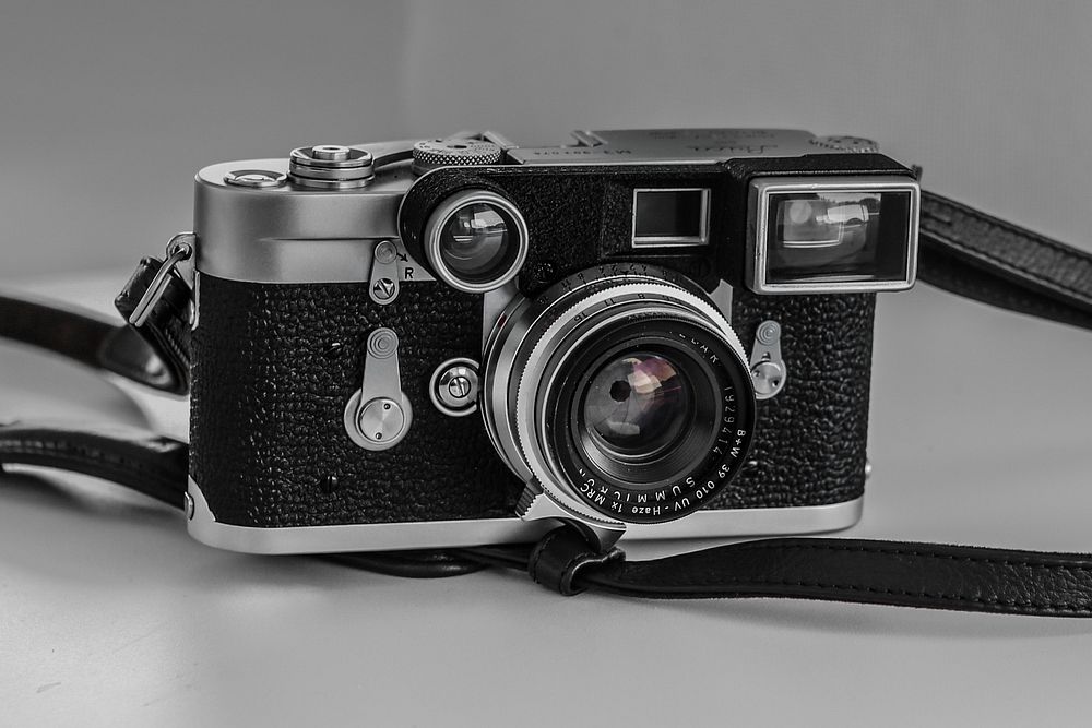 Vintage camera with leather black strap on a white surface. Original public domain image from Wikimedia Commons