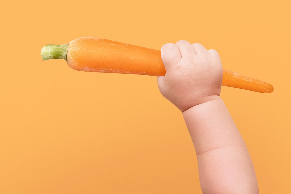 Baby hands psd holding carrot on orange background