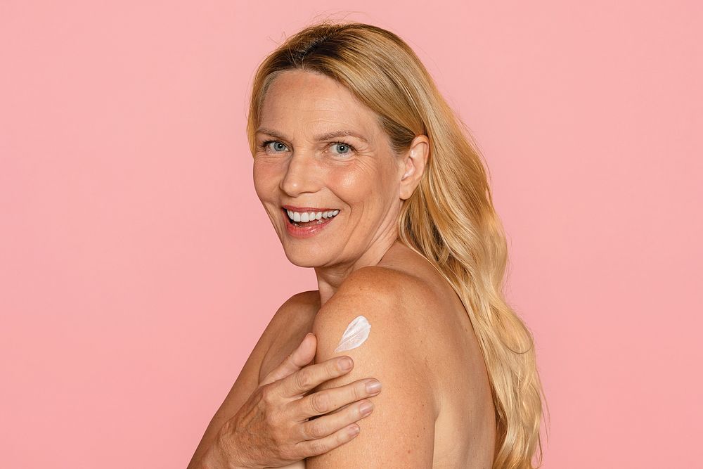 Woman putting on body lotion, pink background