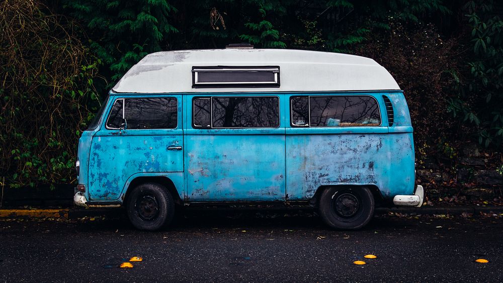 An old blue camper van with a white top parked on the side of the road. Original public domain image from Wikimedia Commons