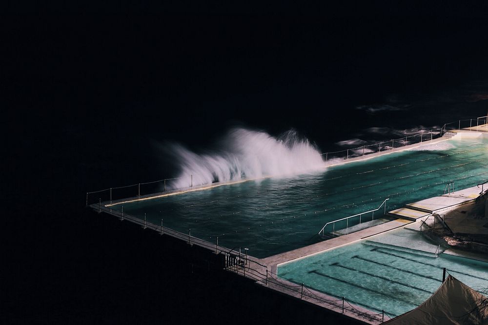 Bondi Beach at night with waves from the ocean splashing into it. Original public domain image from Wikimedia Commons
