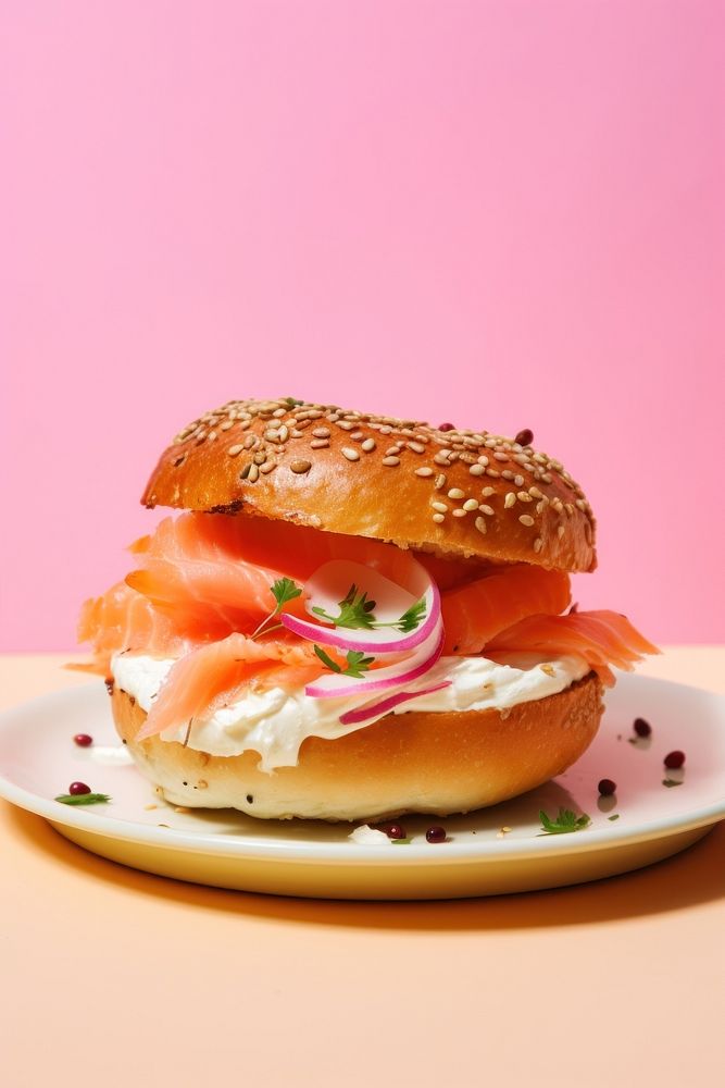 Bagel with creamcheese and salmon cut in half served on pink paper burger bread plate.