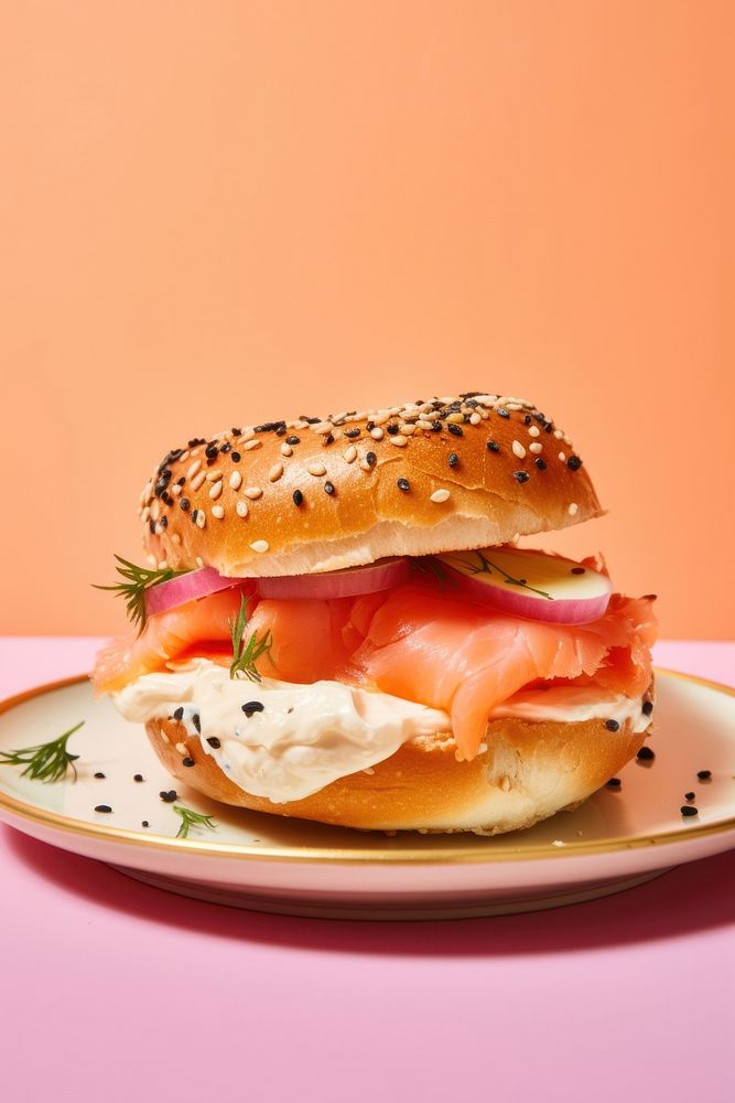 Bagel with creamcheese and salmon cut in half served on pink paper burger bread plate.