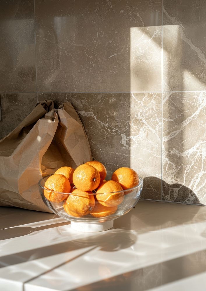 Kitchen counter from the front view with a glass bowl full of oranges and a paper brown bag produce fruit plant.