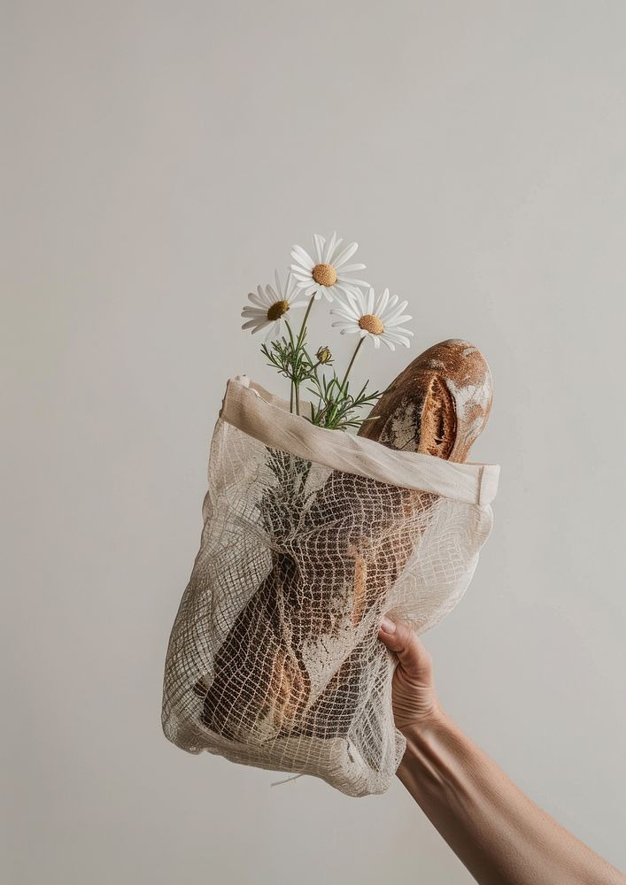 A hand holds a mesh net bag with a flower and bread inside handicraft blossom plant.