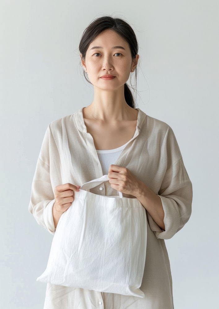 Asian woman in 50s wearing linen shirt holding a white tote bag mock up clothing knitwear apparel.