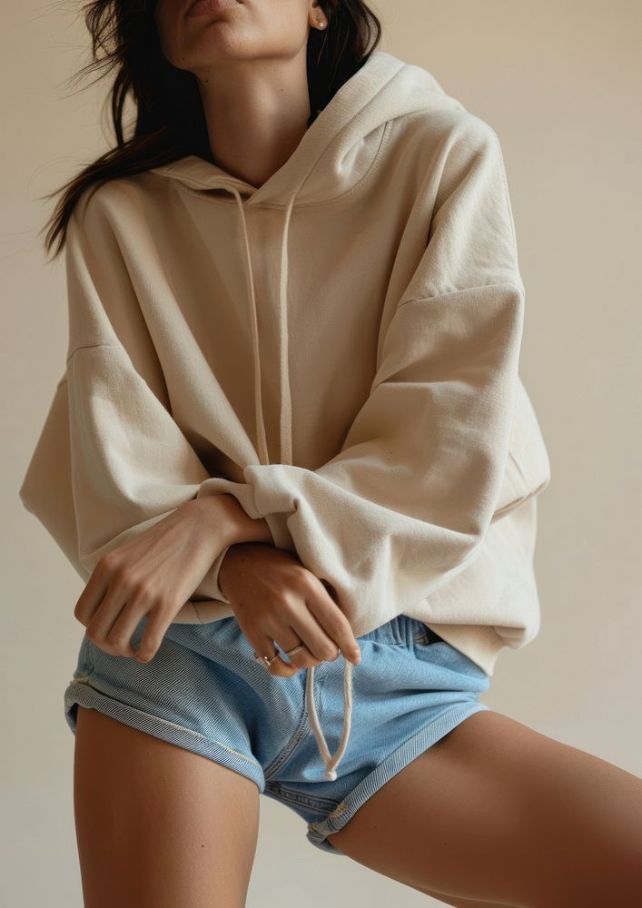 A woman in the studio showing off her blue shorts and beige oversized hoodie sweatshirt beachwear clothing.