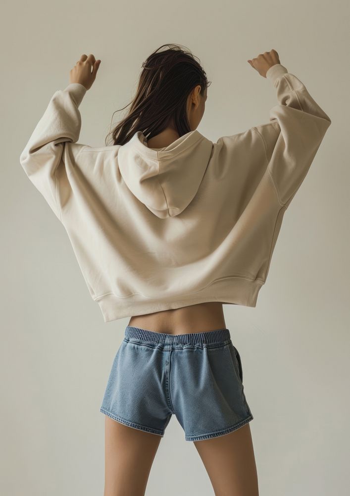 A woman wearing an oversized beige hoodie and blue shorts with a high waistline sweatshirt clothing knitwear.