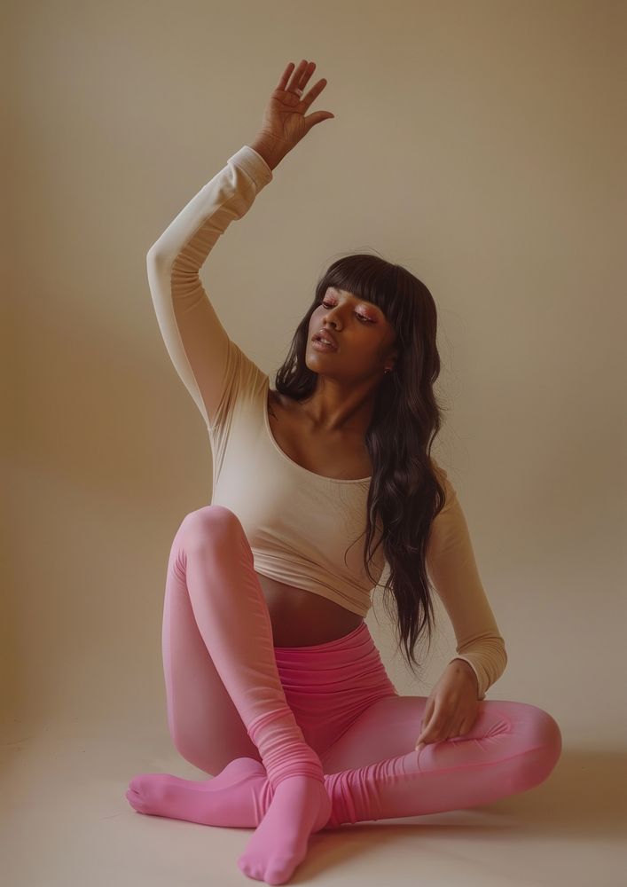 An attractive woman sitting on the floor wearing pink tights and a long-sleeved top clothing exercise apparel.