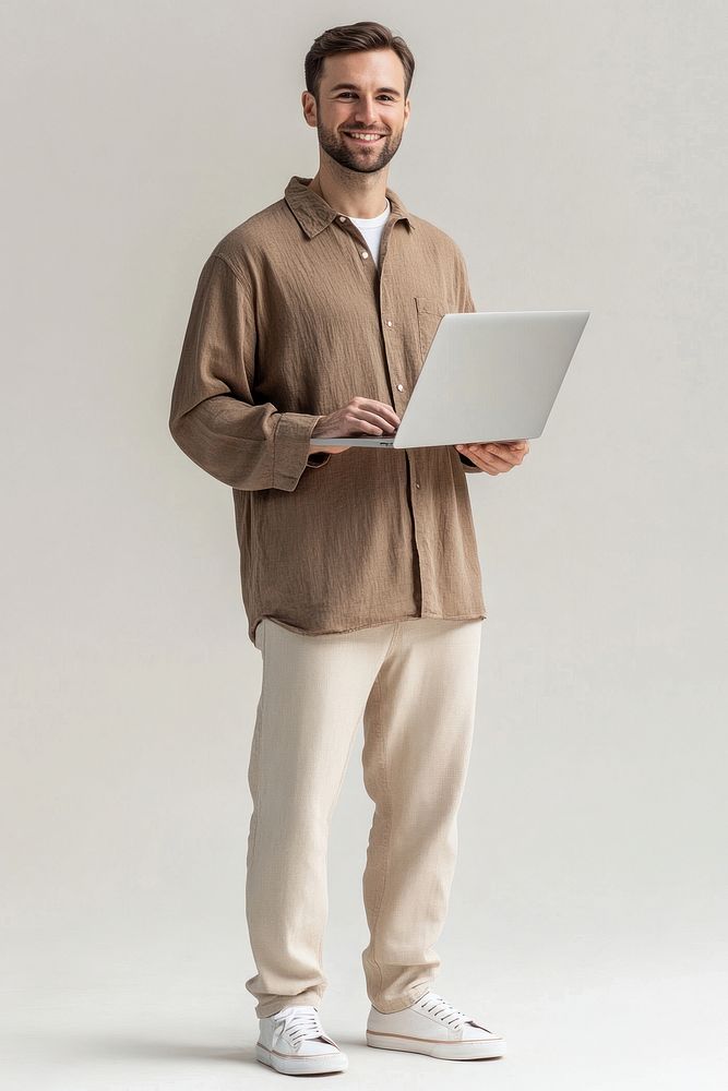 An american man wearing an oversized brown shirt with beige trousers and sneakers standing laptop background.