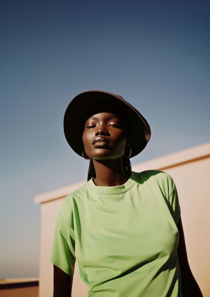 A black teenage woman face the sunlight wearing minimal green hat fashion adult portrait.