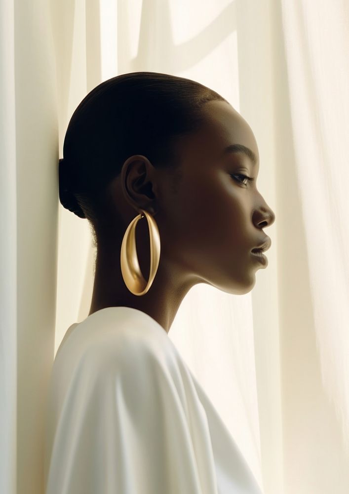 A black woman poke her head out of the white curtains wearing modern gold earring photography portrait jewelry.