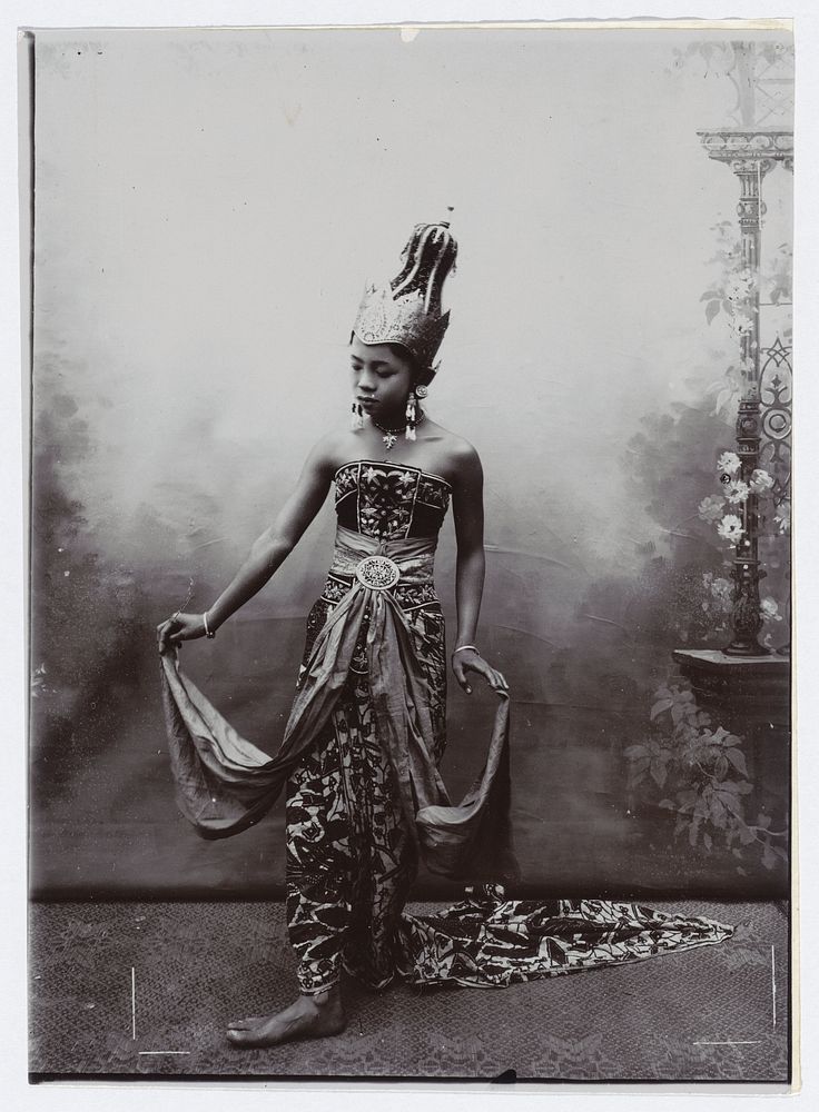 Studioportret van een jongevrouw in batik sarong en bewerkte bovenkleding, op haar hoofd draagt zij een kroon gelijkend…