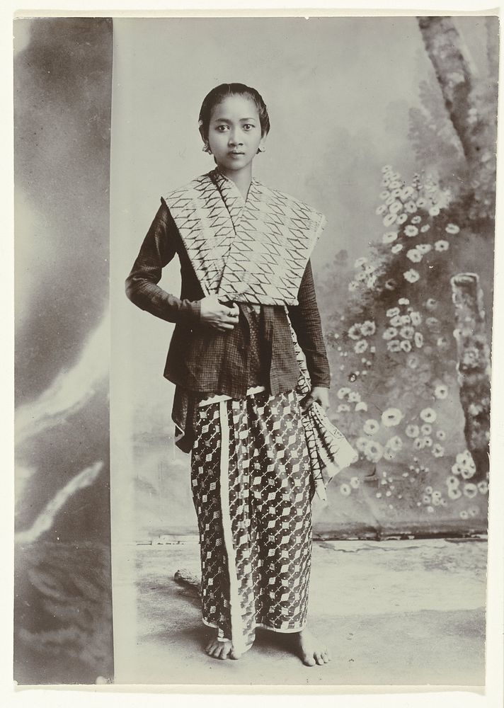 Studioportret van een jonge Javaanse vrouw in een sarong met batik motief en een overhemd met ruitjes patroon (c. 1867 - c.…