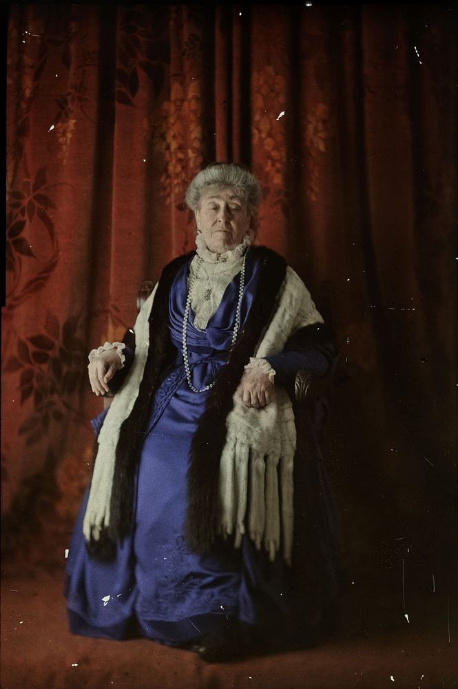 Portret van een vrouw in blauwe jurk op stoel tegen rode achtergrond (1907 - 1935) by anonymous