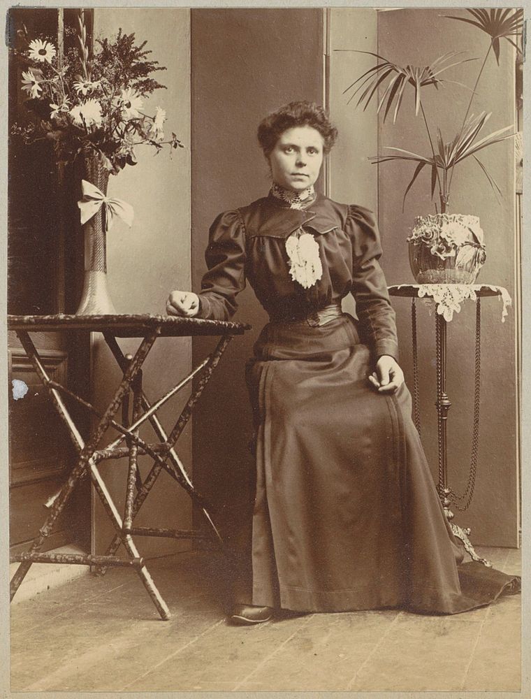 Vrouw zittend in een serre bij tafels met bloemen en planten (c. 1900 - c. 1910) by anonymous