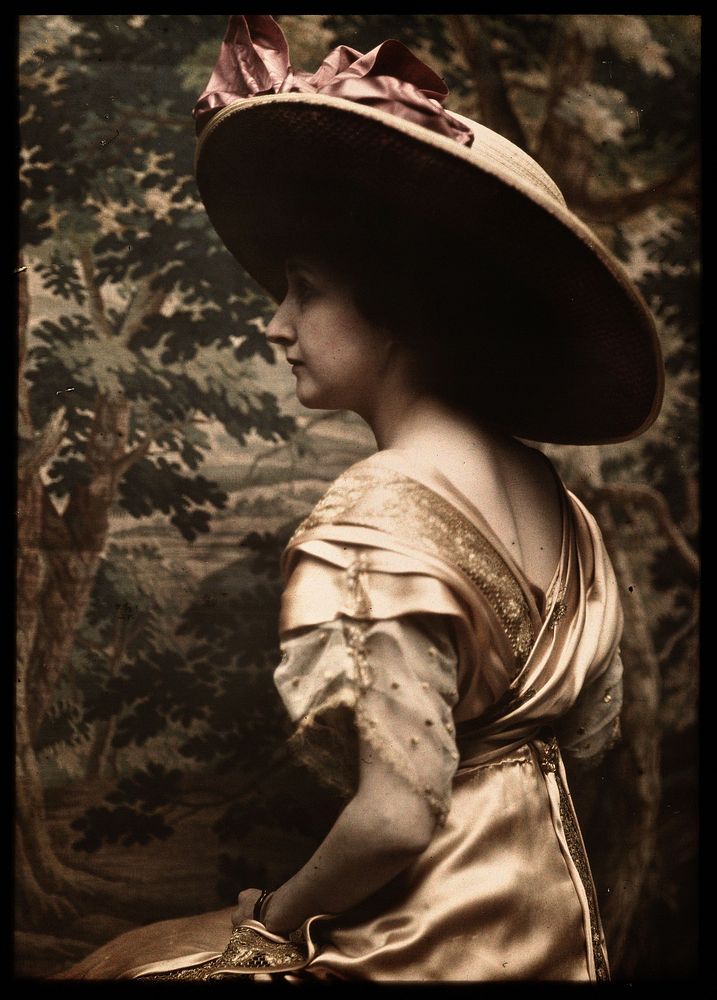 Portret van een vrouw met hoed, zittend voor een wandtapijt met landschap (1910) by Francis Bruguière