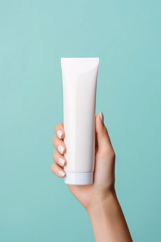 Hand holding squeeze bottle plastic tube container of cream milk toothpaste cosmetics.