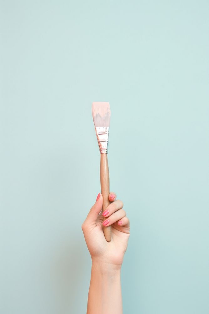 Hand holds a paint brush toothbrush holding spatula.