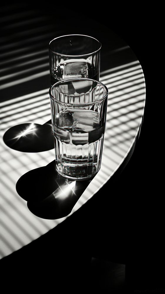 Drinking glasses on table reflect sunlight monochrome black white.
