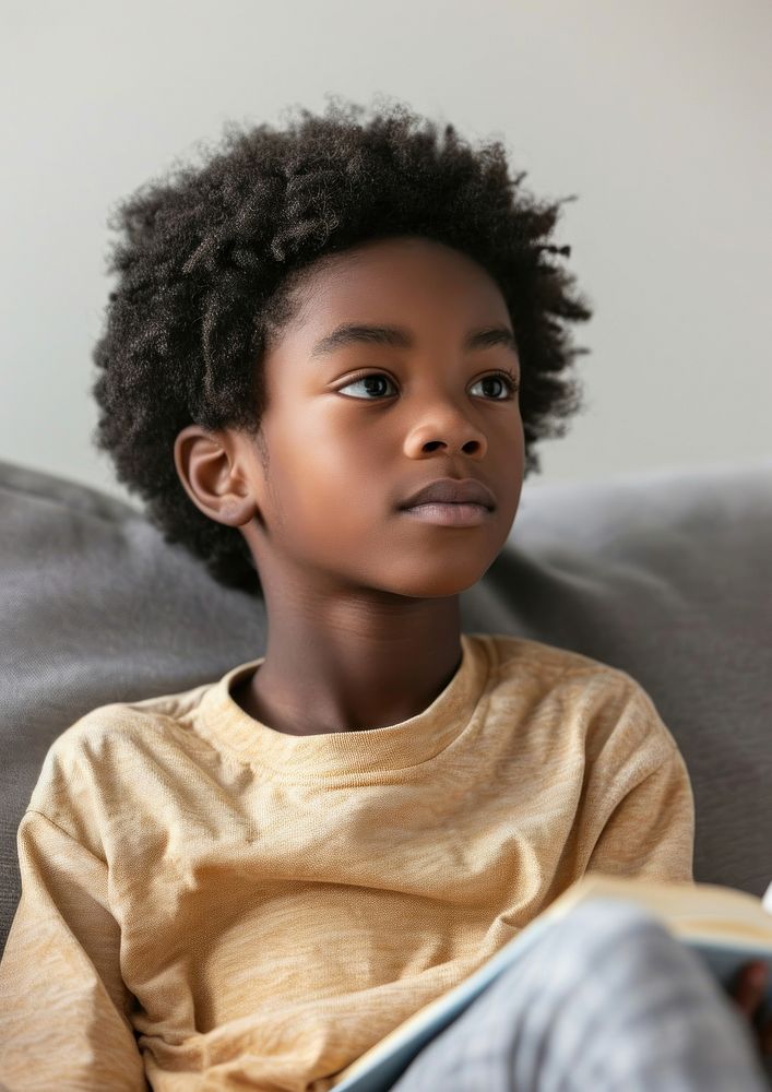 A cute african american boy on sofa child book contemplation.