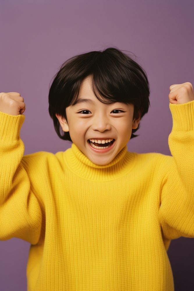 Asian boy with his hands up laughing sweater yellow.