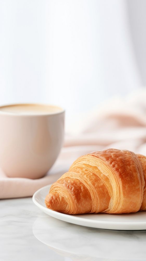 A croissant sitting on top of a cup of coffee bread food viennoiserie.