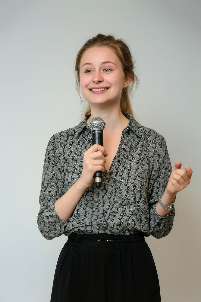 A woman lecturer holding a microphone at waist level portrait clothing smiling.