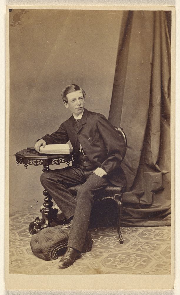 Unidentified young man seated at a table with a book on top by A Melliss