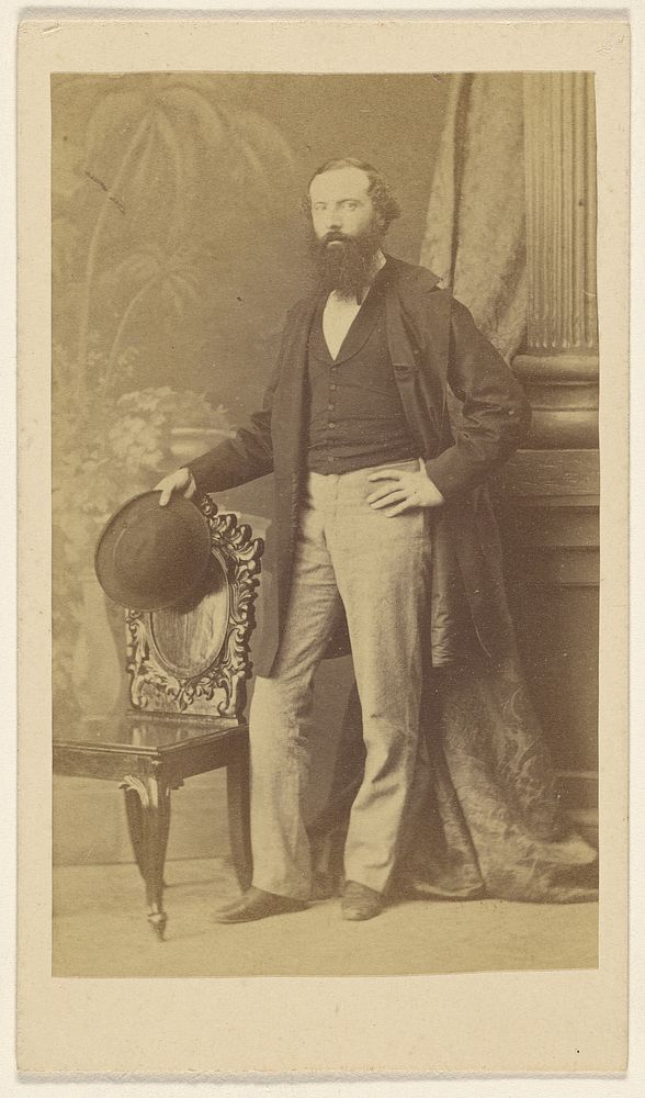 Unidentified bearded man standing with one hand on hip, the other with hat in hand on chair back by F Schwarzschild