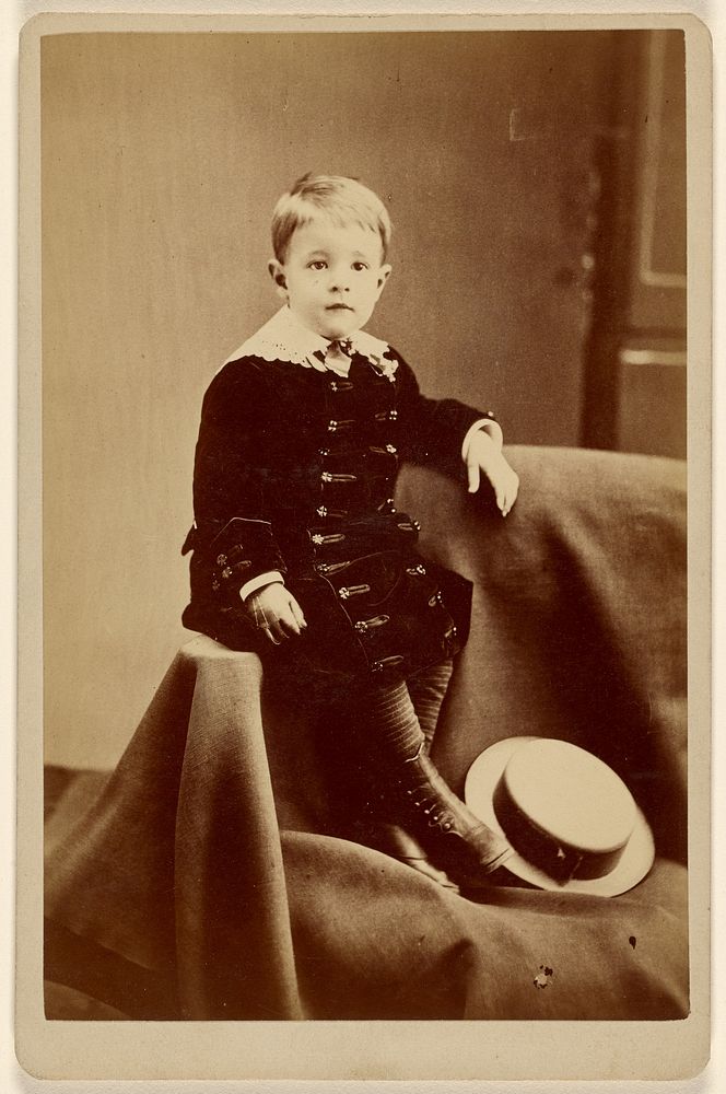 Little boy, seated on cloth, straw hat at feet