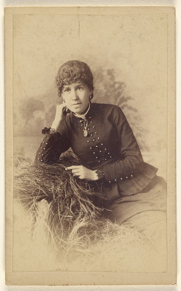 Unidentified woman seated with hand on cheek, posed on a pile of hay by Miller and Company