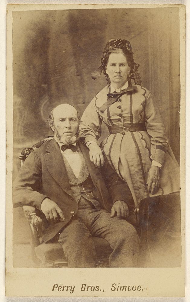 Unidentified couple: bearded man, seated and woman, standing by E B Perry Brothers