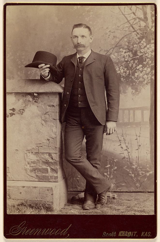 Studio portrait of a man holding a hat by W H Greenwood