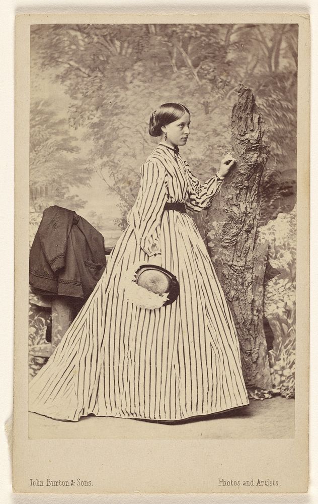 Unidentified woman wearing a striped dress, holding a hat, standing by John Burton and Sons