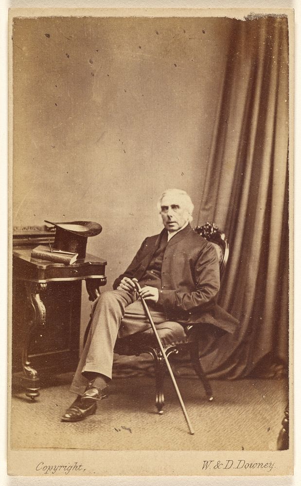 Unidentified white-haired man seated, holding a cane, top hat and book on table at left by W and D Downey