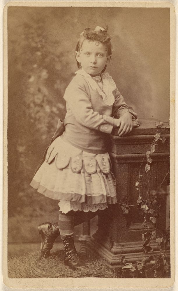 Unidentified little girl, standing, leaning on a studio prop by Lee Stearns