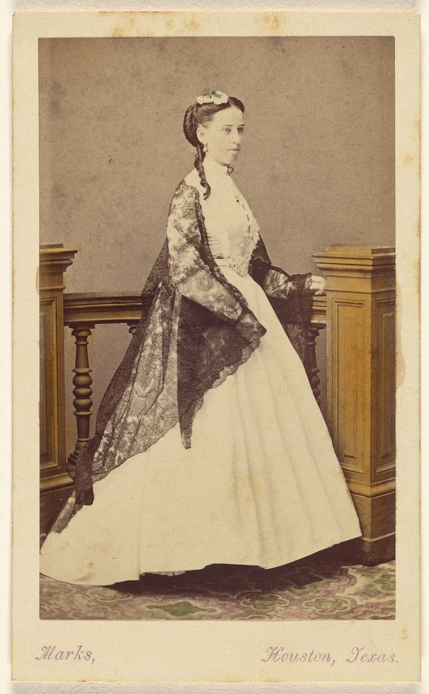 Unidentified woman wearing a white dress and black shawl, standing by Harvey R Marks