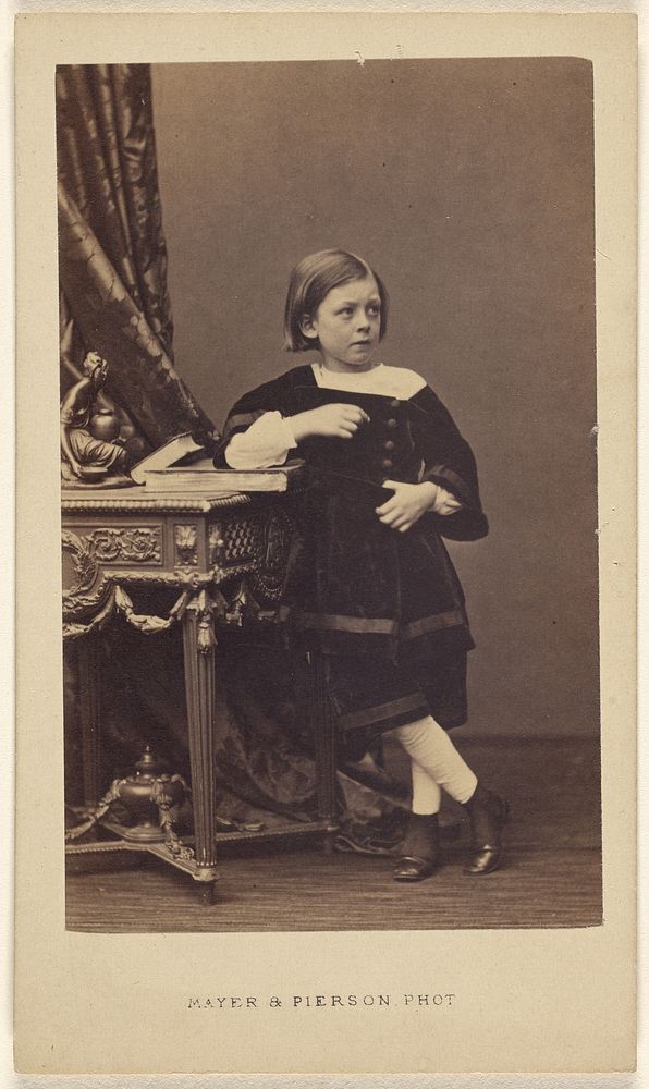 Unidentified little girl standing, elbow on top of a closed book on a table by Mayer and Pierson