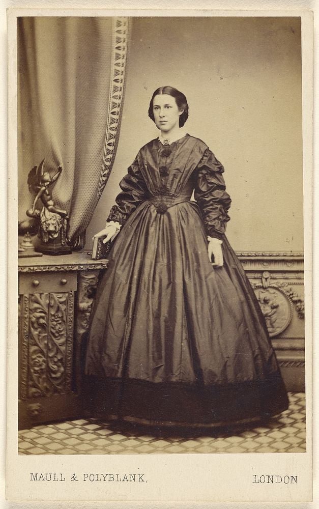 Unidentified woman wearing a long dress, holding a book atop a credenza, standing by Maull and Polyblank