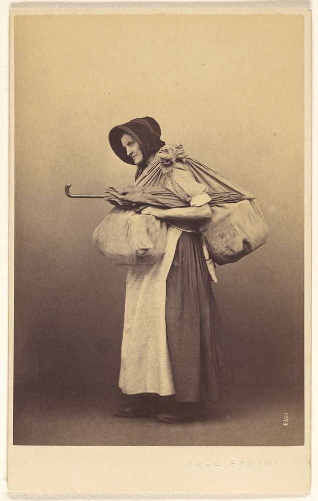Unidentified woman wearing a bonnet standing, with two bundles over her shoulder plus an umbrella by Thomas Edge