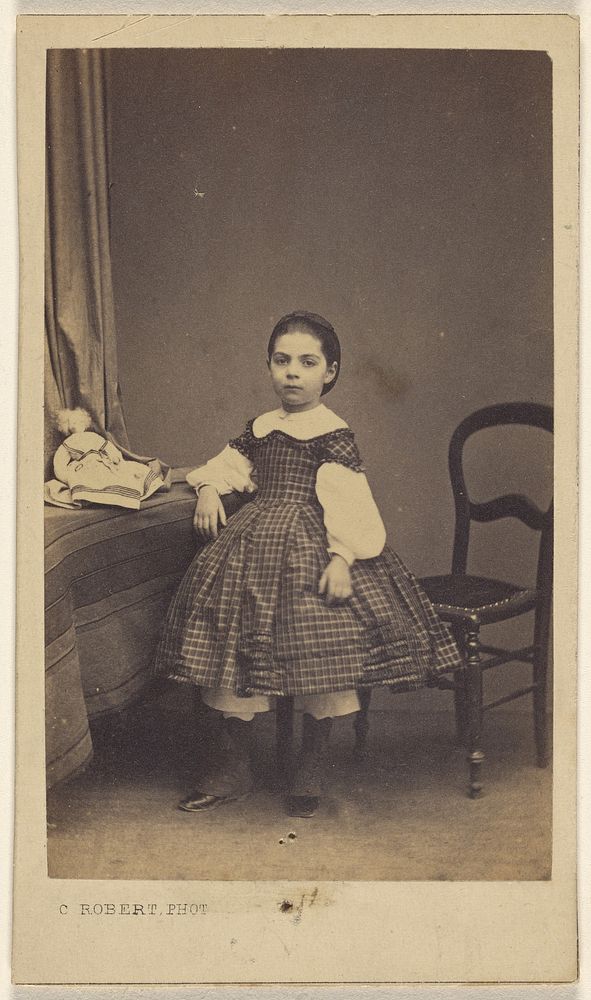 Unidentified little girl standing, with elbow on table by C Robert
