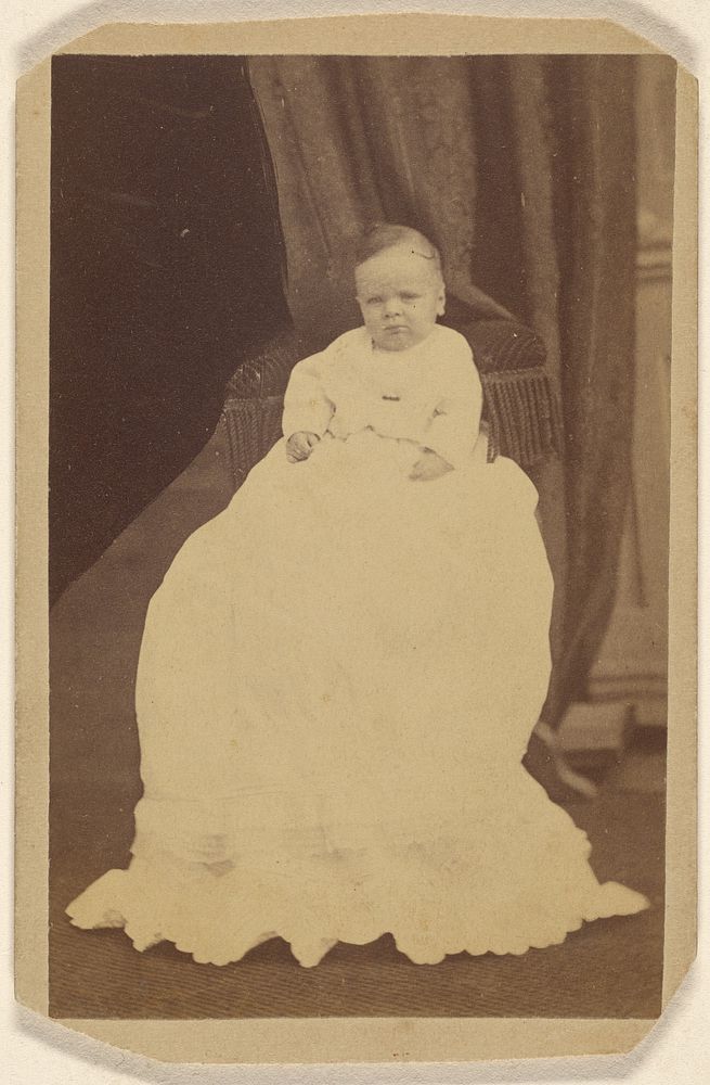 Unidentified baby wearing a long gown, seated on a couch by Peter S Weaver