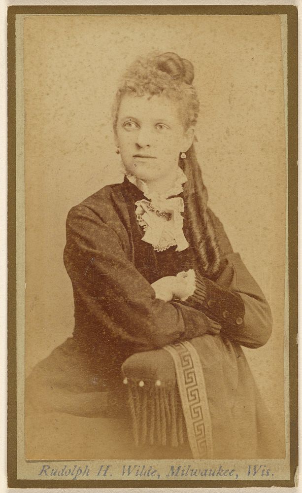 Unidentified woman seated with arms crossed on chair arm by Rudolph H Wilde