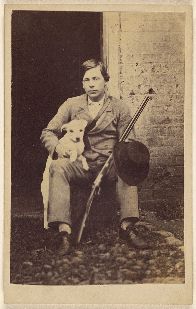 Man seated with a white dog, a rifle and hat leaning on his leg
